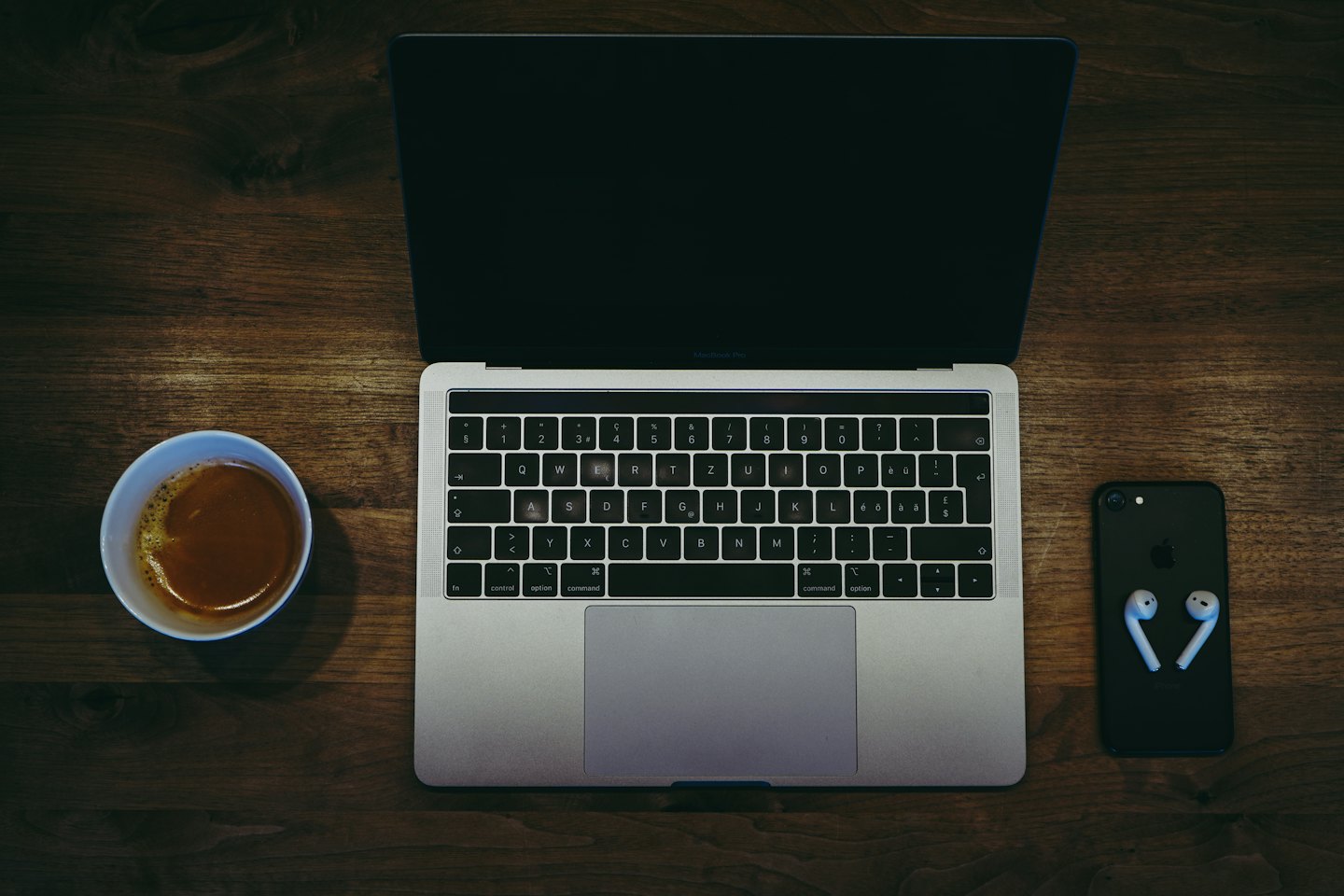 Laptop, coffee, and phone on a dark wooden desk.