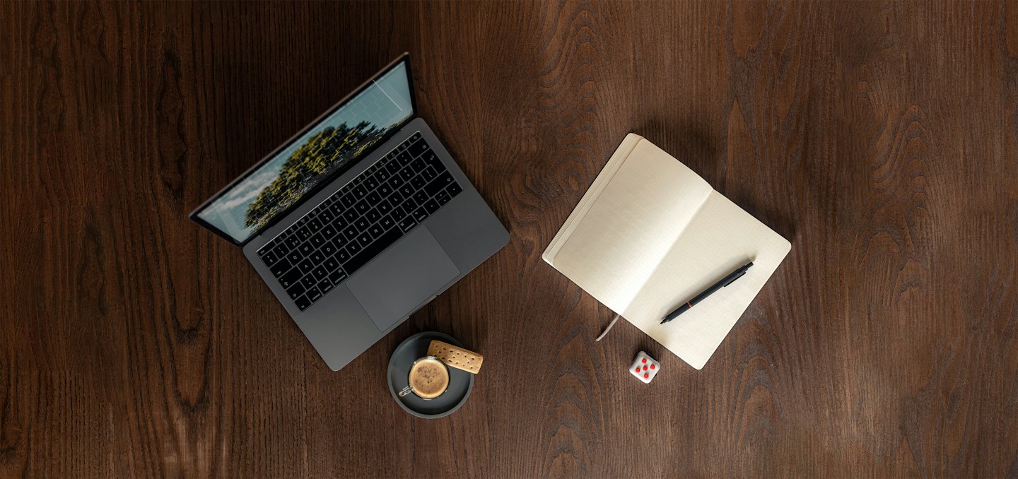 Laptop, notebook, and coffee sit on a wooden desk.